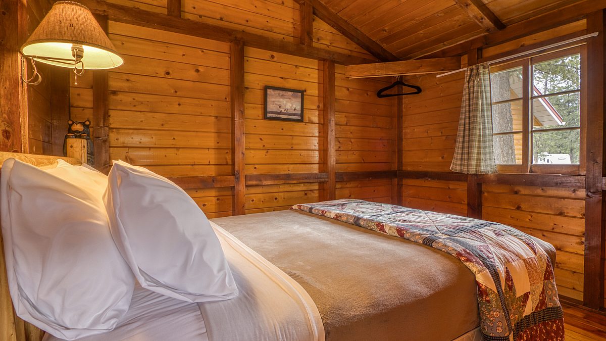 Queen bedroom in wood panelled cabin. Lamp and blanket.