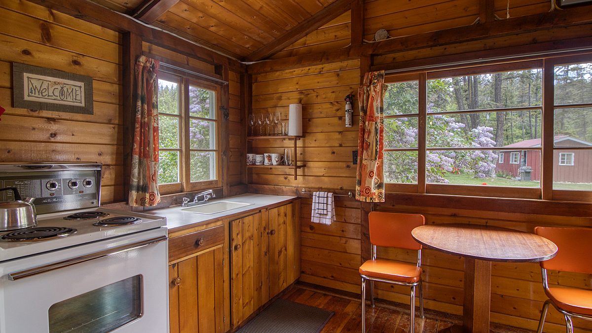 Wood panelled kitchen area with small dining table, two chairs, and oven to the right.