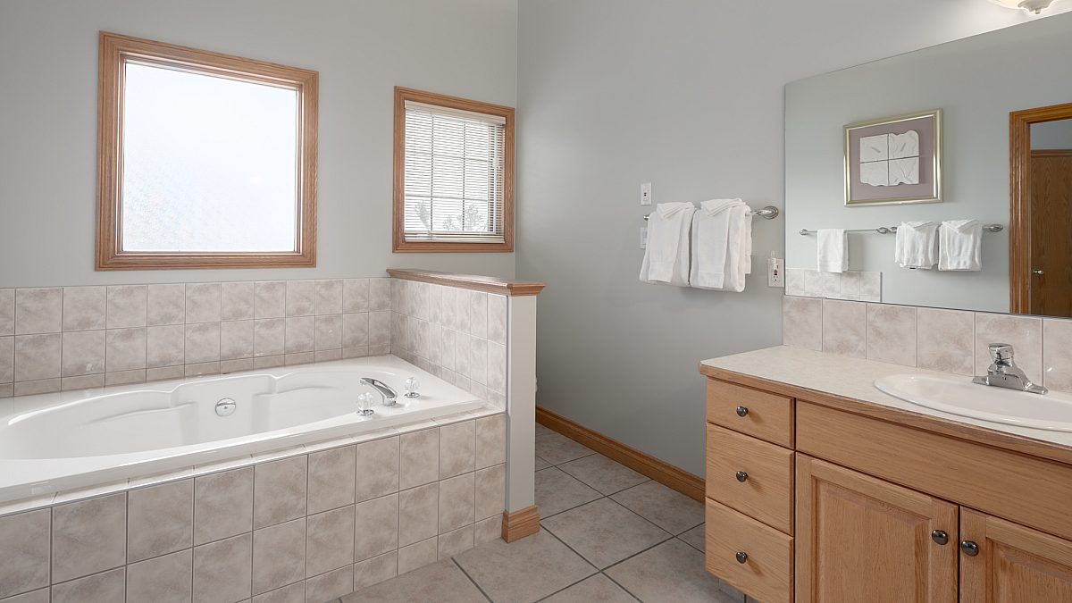Ensuite bathroom with bathtub, vanity, mirror, and sink.