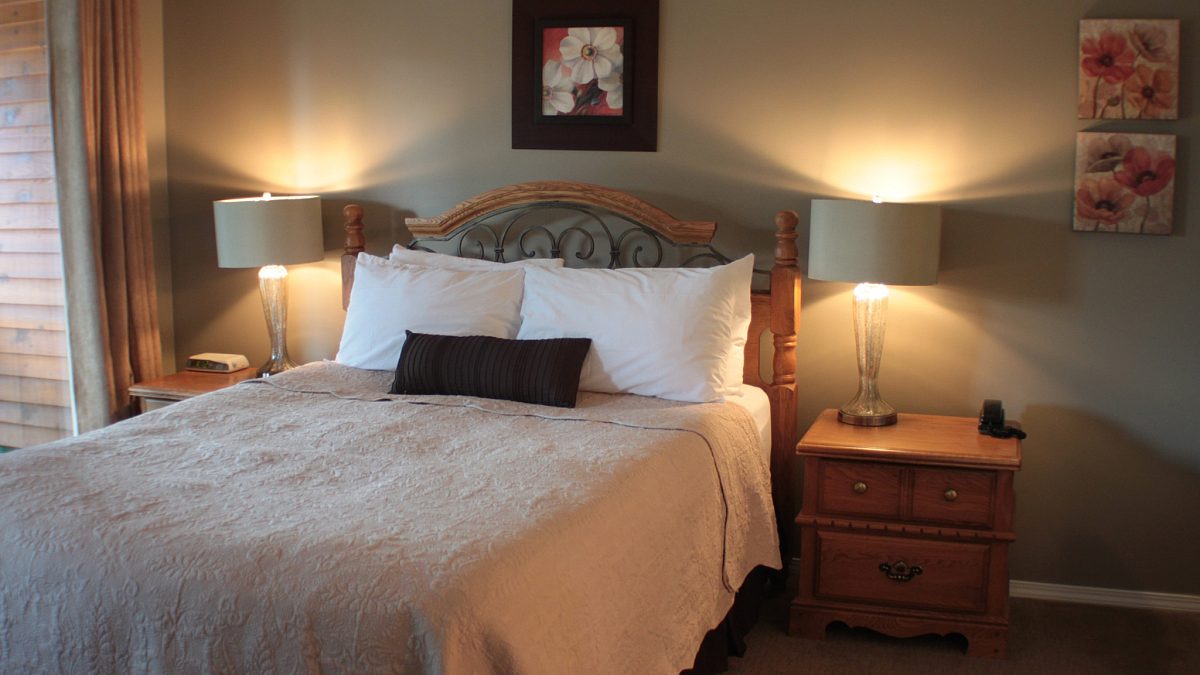 Master bedroom with queen bed, beige bedding, two night tables and lamps.