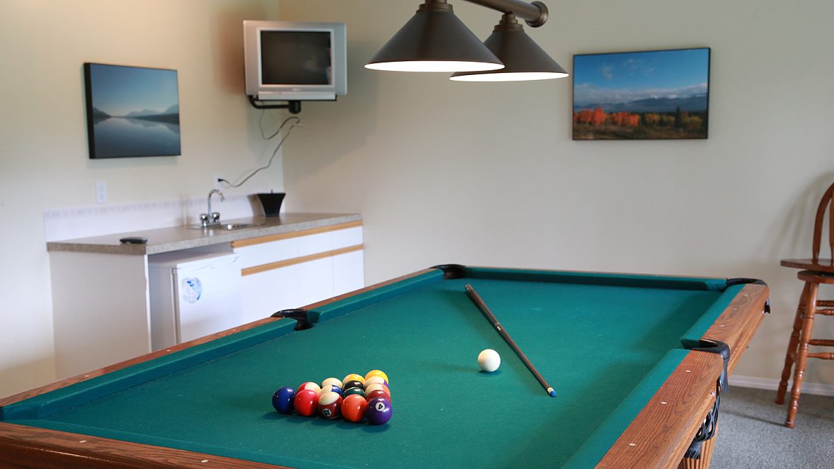 Pool table and recreation room. Balls and sticks on pool table, dresser, window, and paintings.