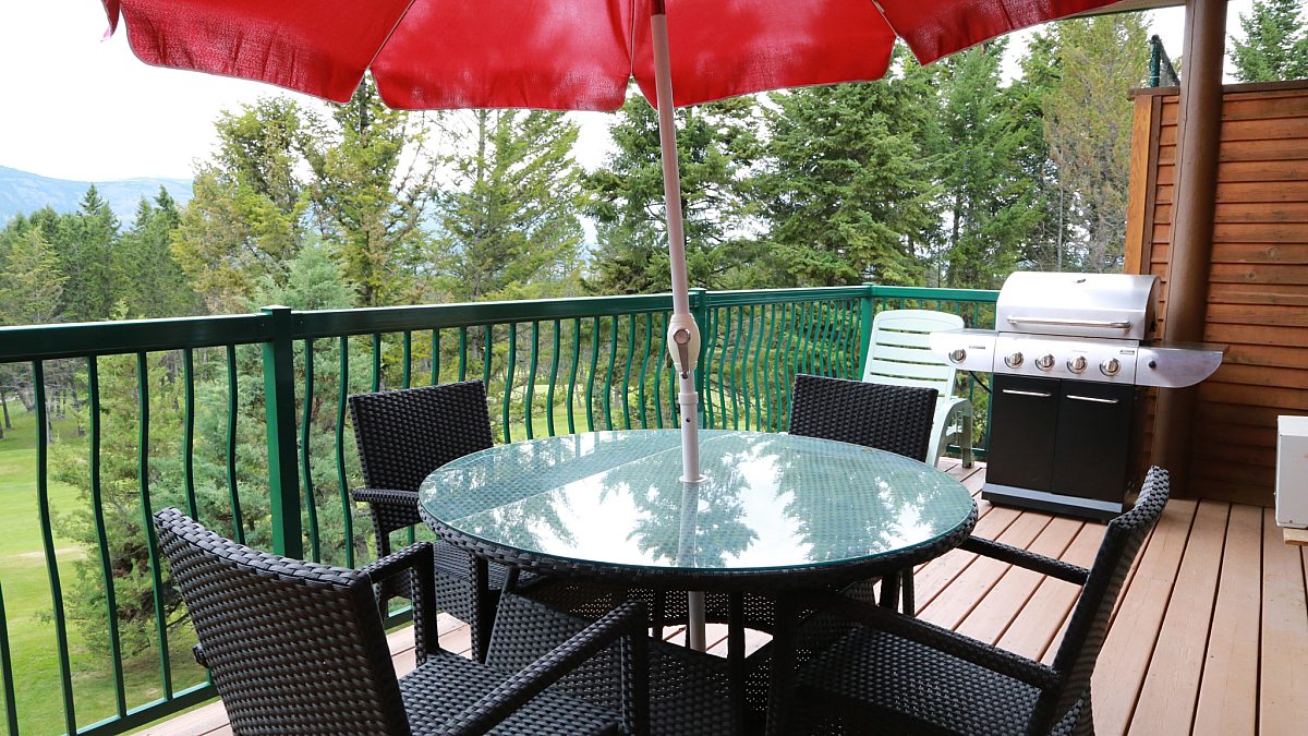 Patio furniture with table, chairs, and red umbrella. BBQ in distance.