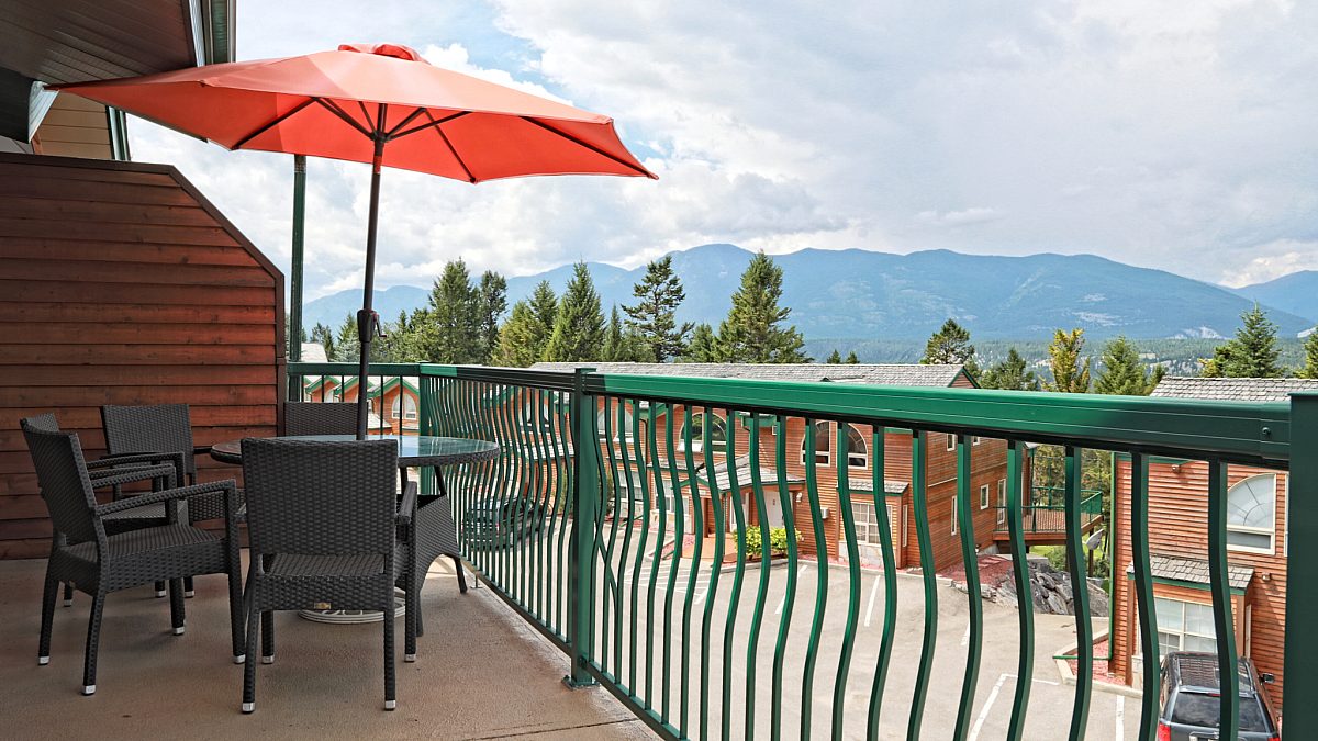 Deck with patio furniture, umbrella, and green railing overlooking other accommodations and mountains.