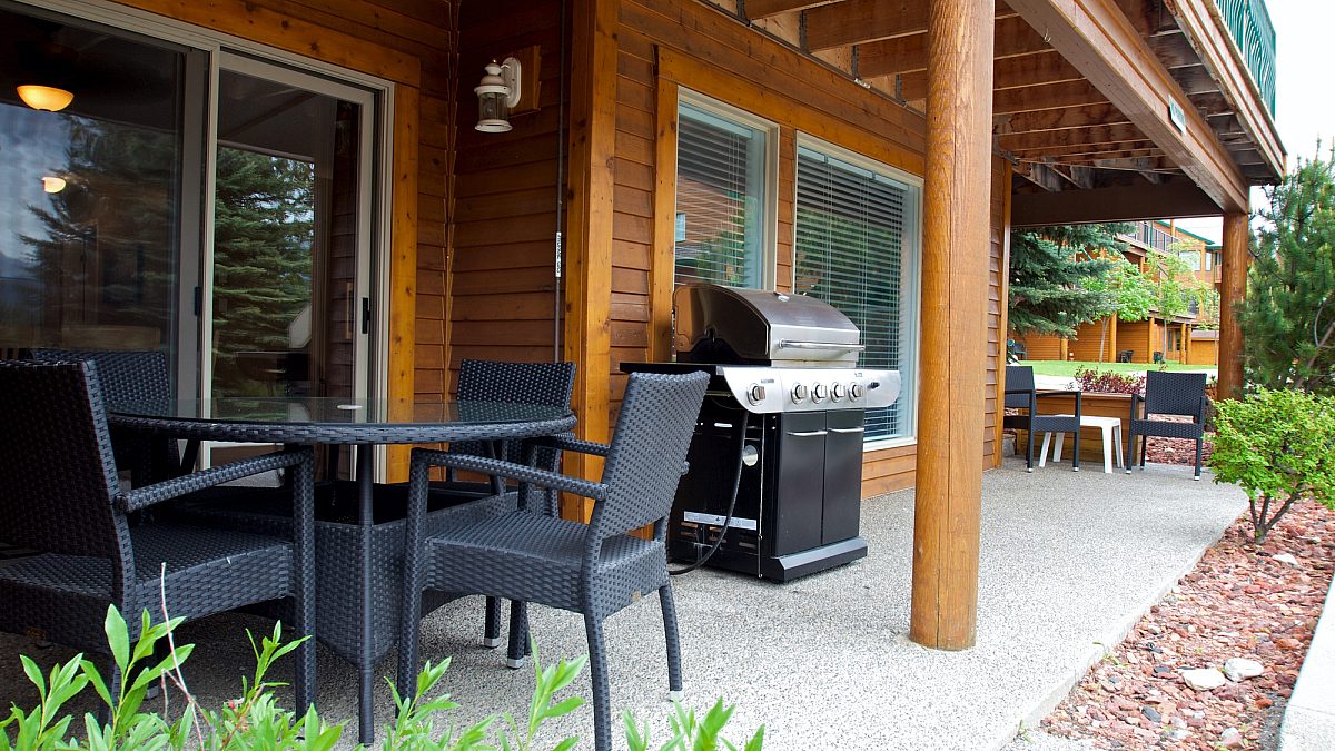 Deck with barbecue, patio furniture. Paved patio area with greenery surrounding.