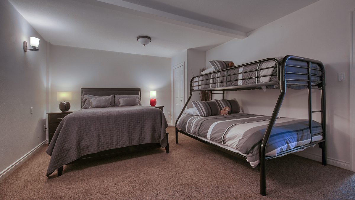 Bedroom with double bed and bunk bed. Grey bedding and two bedside tables with lamps.