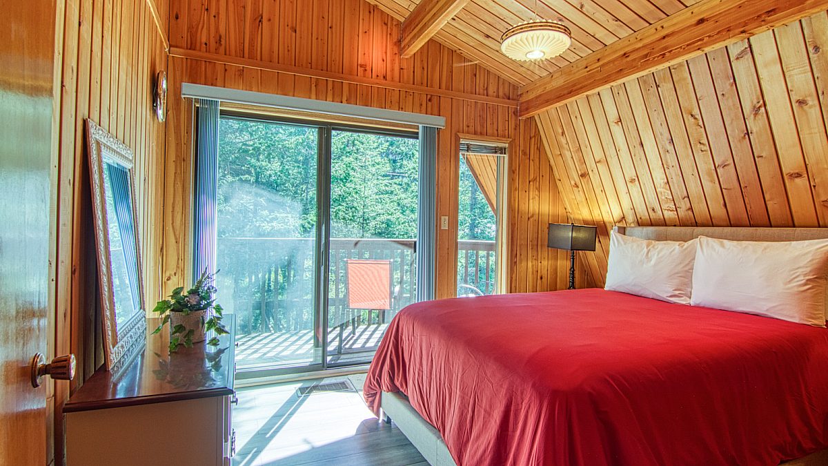 Bedroom with queen bed with red bedding. Wood panels on the walls and doors to patio.