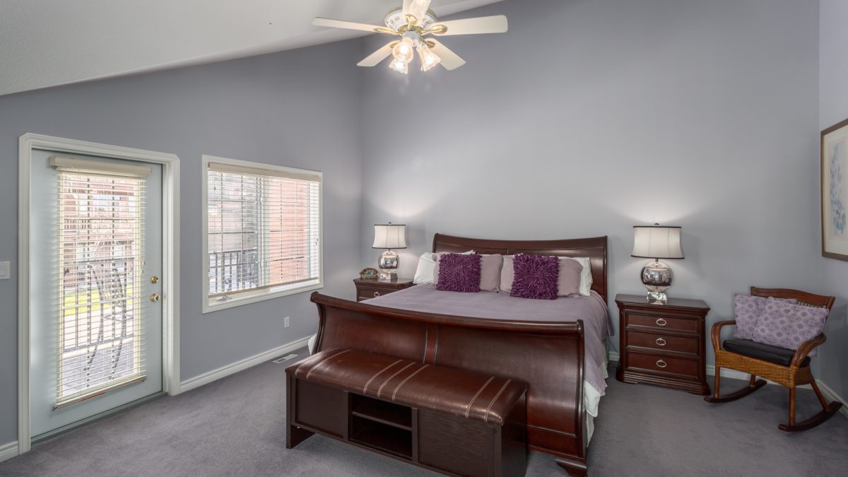 Master bedroom with king bed. Grey walls and high ceiling, two bedside tables with lamps.