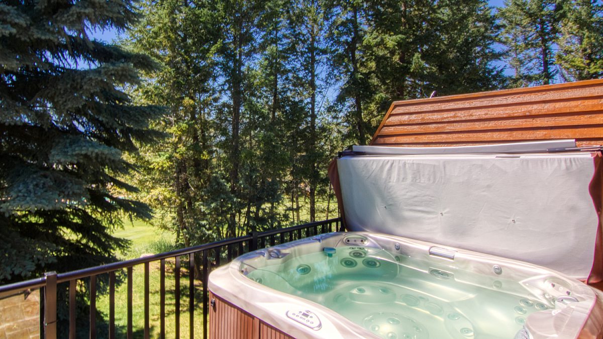 Wood paneled porch hot tub on a deck with its lid off. The water in the hot tub is clear. Porch overlooks treed area.
