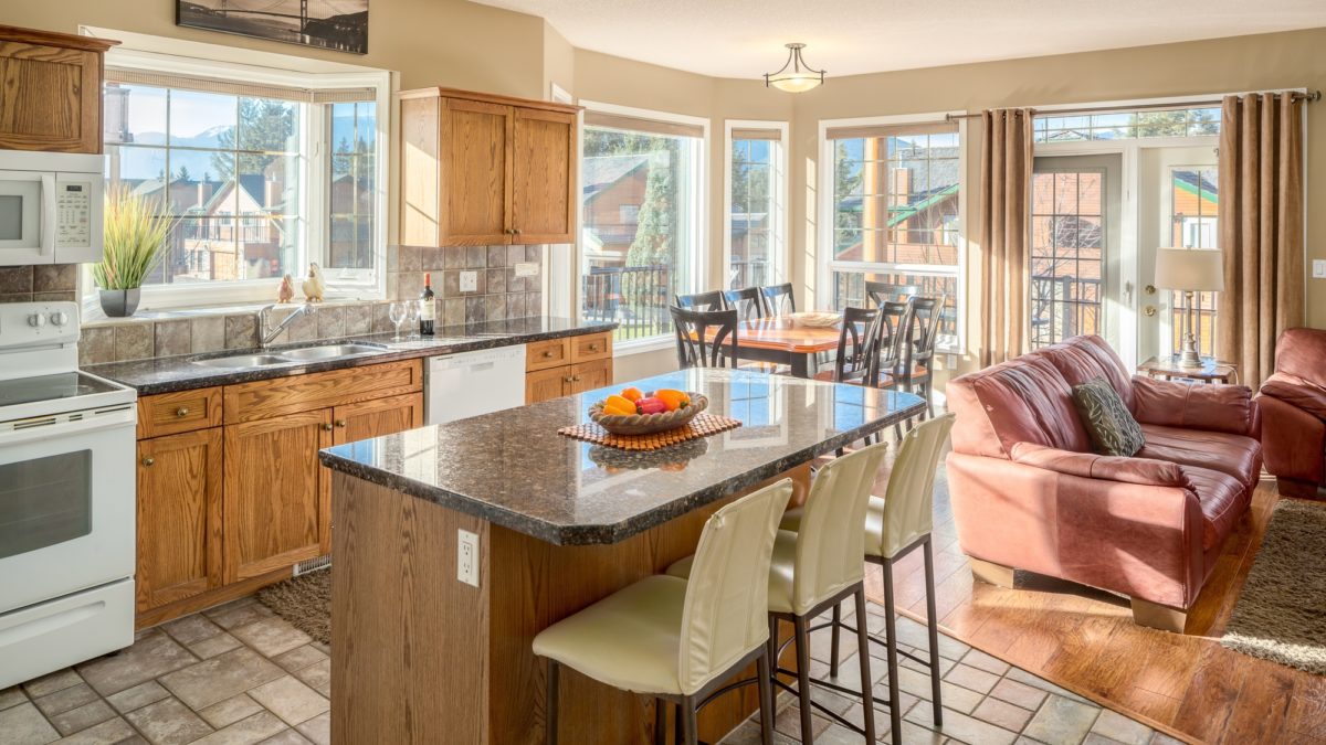 Kitchen with ample lighting and windows. Island with barstool seating. Living room to the left.