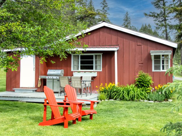 Small red cabin with two red outdoor lounge chairs outside. Trees and greenery surrounding.
