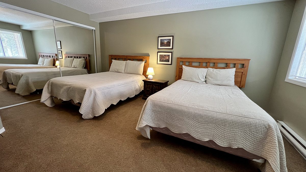 Two double beds with white bedding in a capeted room with light sage walls.