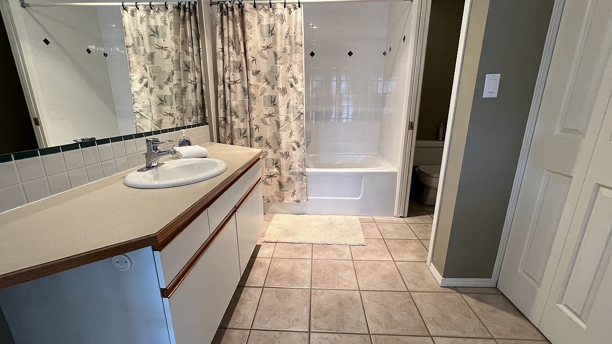 Bathroom with tile flooring, white vanity, mirror, and cupboards.