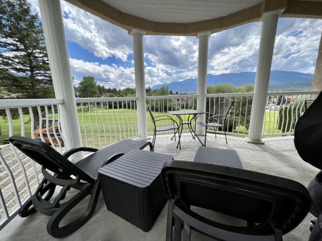 Patio overlooking a golf course, mountains on a mixed sun and cloud day. Two black patio lounge chairs and black metal chairs with a table.